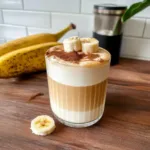 A cozy Banana Bread Latte topped with banana slices and dusted with cinnamon, featuring layered milk and espresso for a rich, bakery-inspired coffee drink.