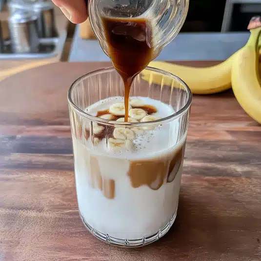 Banana Bread Latte topped with banana slices and dusted with cinnamon, featuring layered milk and espresso for a rich