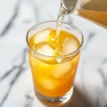 A refreshing glass of the Cortisol Cocktail for Weight Loss filled with ice cubes and a bright orange drink being poured in, perfect for morning hydration and stress balance.