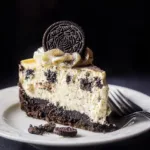 Slice of creamy Baked Oreo Cheesecake with chocolate cookie crust, whipped cream topping, and Oreo cookie garnish on a white plate.