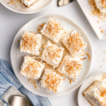 A creamy coconut poke cake topped with fluffy whipped topping and toasted coconut flakes in a white baking dish.