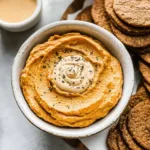 A creamy pumpkin dip in a white bowl topped with whipped spiced pumpkin mixture, surrounded by fresh green apple slices and fall fruits