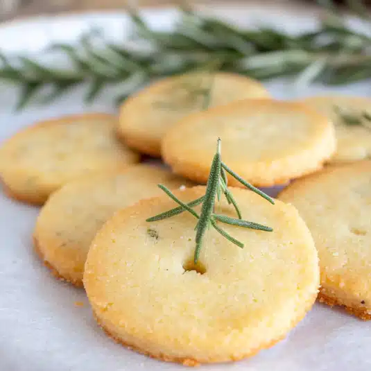 Close-up of golden rosemary shortbread cookies topped with fresh rosemary sprigs, arranged on parchment paper