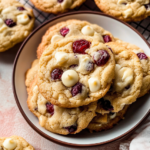 Freshly baked white chocolate cranberry cookies stacked on a plate, showing golden edges, melted white chocolate chips