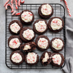 Cooling rack filled with chocolate peppermint cookies topped with white peppermint frosting and crushed candy canes.