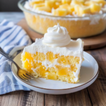 Pineapple poke cake slice with whipped cream topping and pineapple chunks on a plate