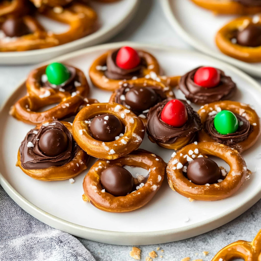 Rolo pretzels topped with melted chocolate, candy pieces, and chocolate candies on a serving plate