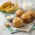 Banana buttermilk muffins with golden domed tops cooling on a wire rack, served with ripe bananas and milk.
