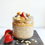 Peanut butter overnight oats in a glass jar topped with strawberries, chia seeds, and oats on a wooden board