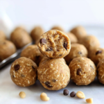 Peanut butter protein balls made with oats and chocolate chips, stacked on a plate with one cut open to show the soft center