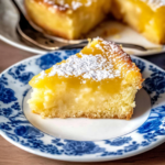 Slice of lemon gooey butter cake with creamy center and golden crust topped with powdered sugar on a plate