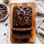 Ultra moist double chocolate banana bread topped with chocolate chips and sliced on a wooden serving board.